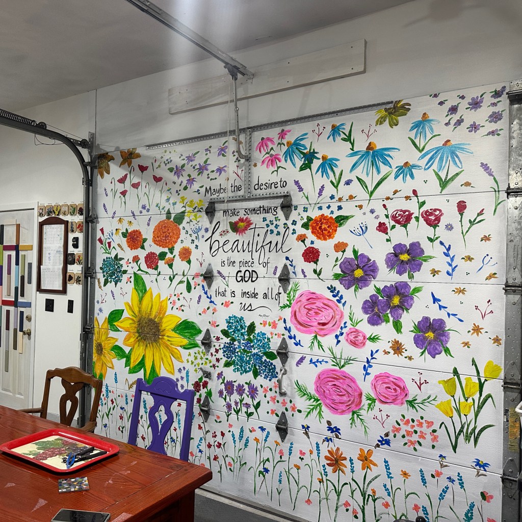 A vibrant mural featuring colorful flowers and an inspirational quote about beauty on a garage door in a workshop setting.